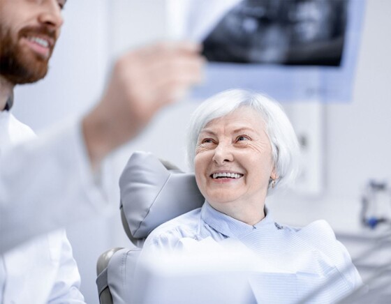 Ältere Patientin sitzt auf einem Behandlungsstuhl und lächelt